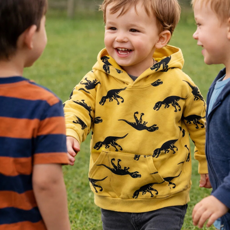 Child smiling in a yellow dinosaur hoodie beside two other children outdoors