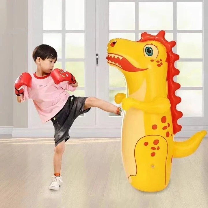 Child wearing boxing gloves and kicking a yellow dinosaur punching bag indoors