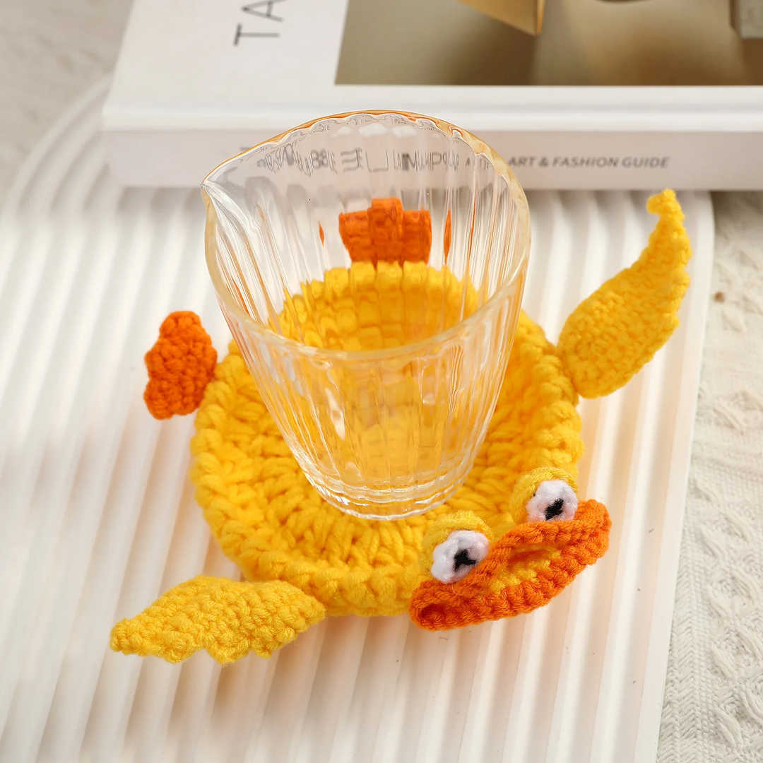 Clear drinking glass resting on a yellow crocheted duck coaster with an orange bill