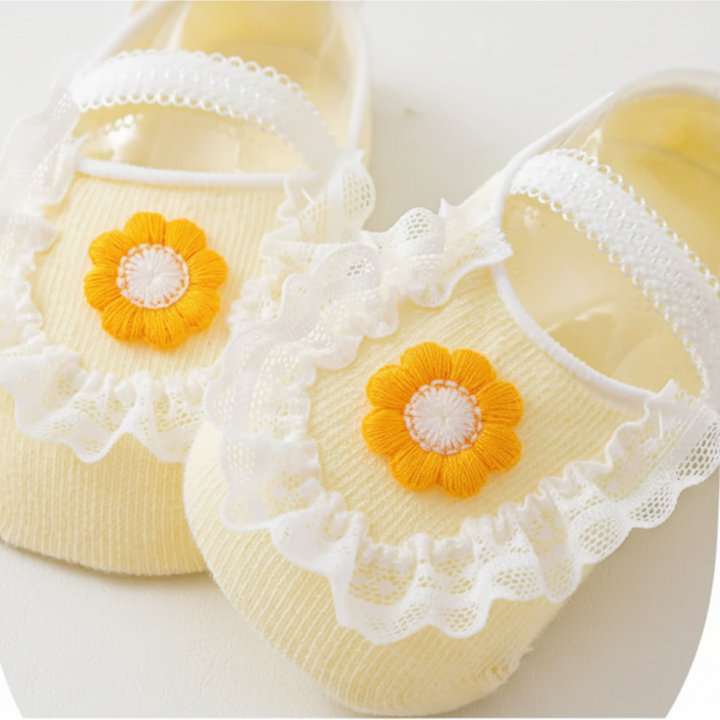 Yellow baby socks with daisy-style flowers, white lace edging and bands across the feet