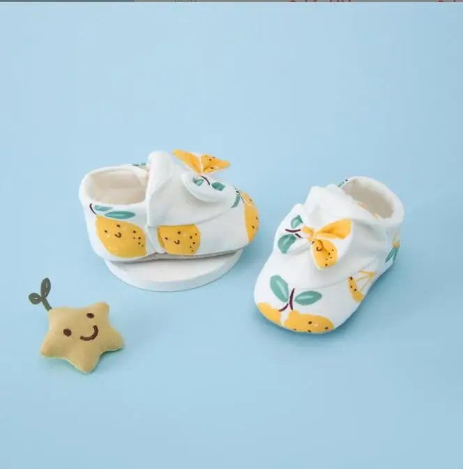 White baby shoes with yellow fruit prints and bow details, shown from the side and front