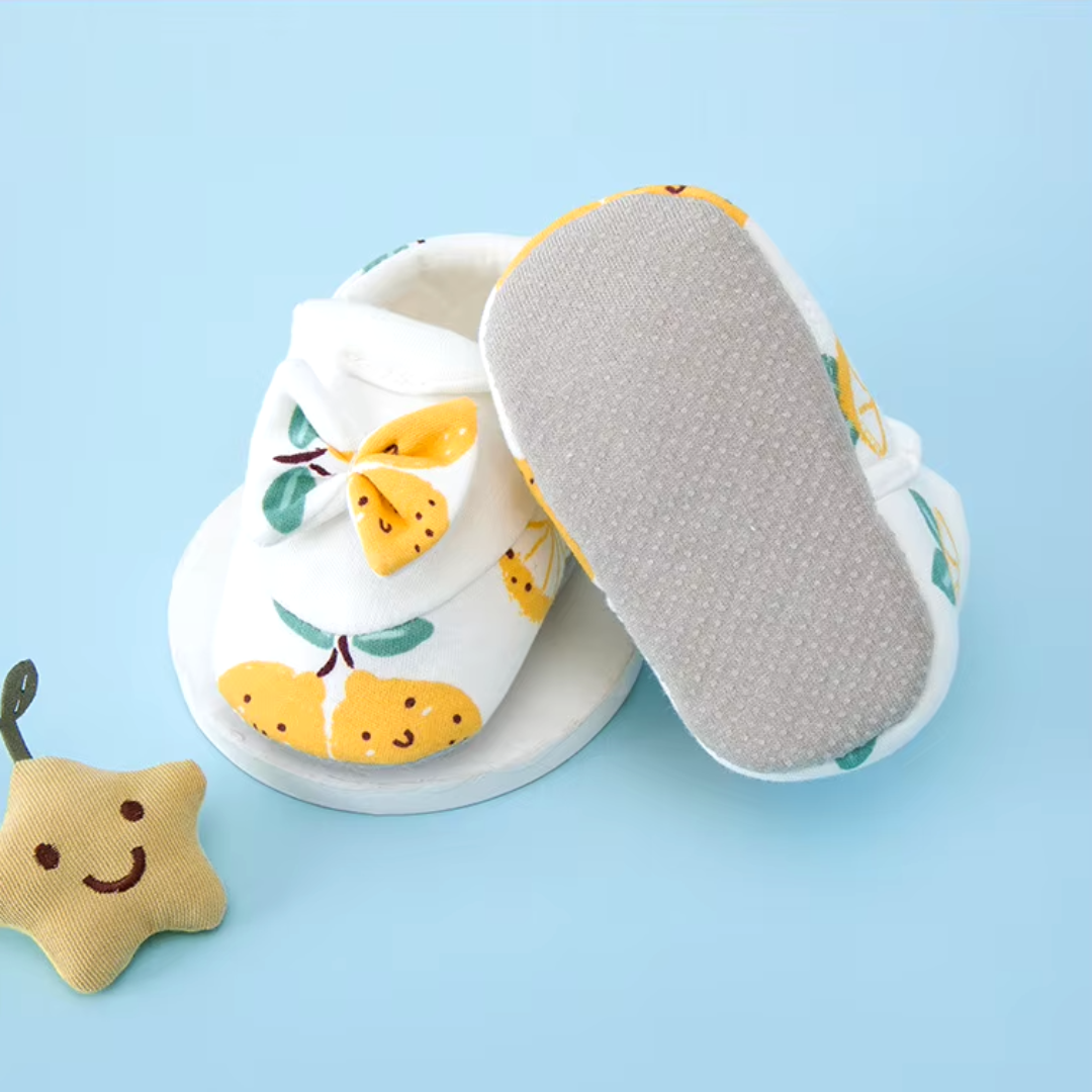 Yellow fruit-print baby shoes with one turned over to show the textured sole
