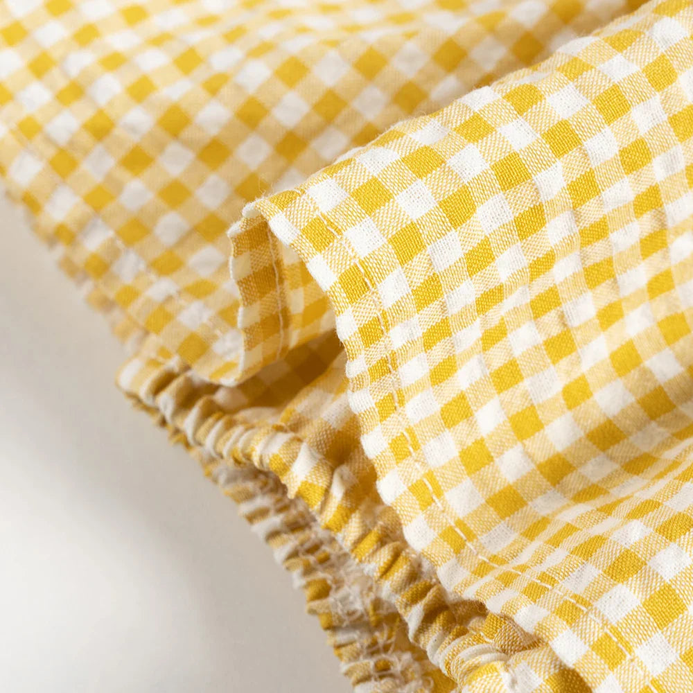 Yellow gingham romper with a gathered elastic leg opening beneath the skirt