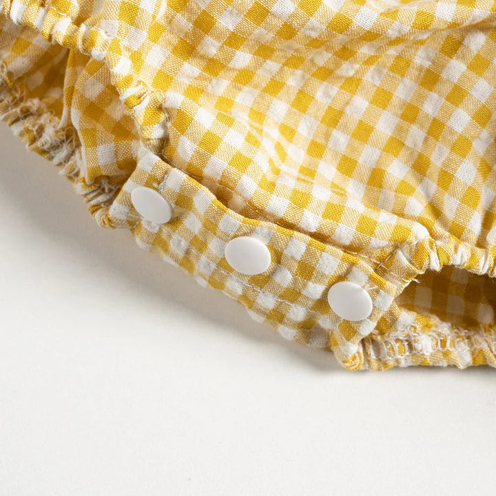 Three white snaps at the crotch of the yellow gingham baby romper