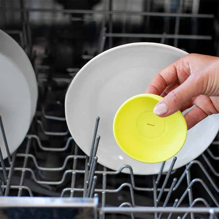 Hand placing a yellow silicone ice cream holder in a dishwasher rack