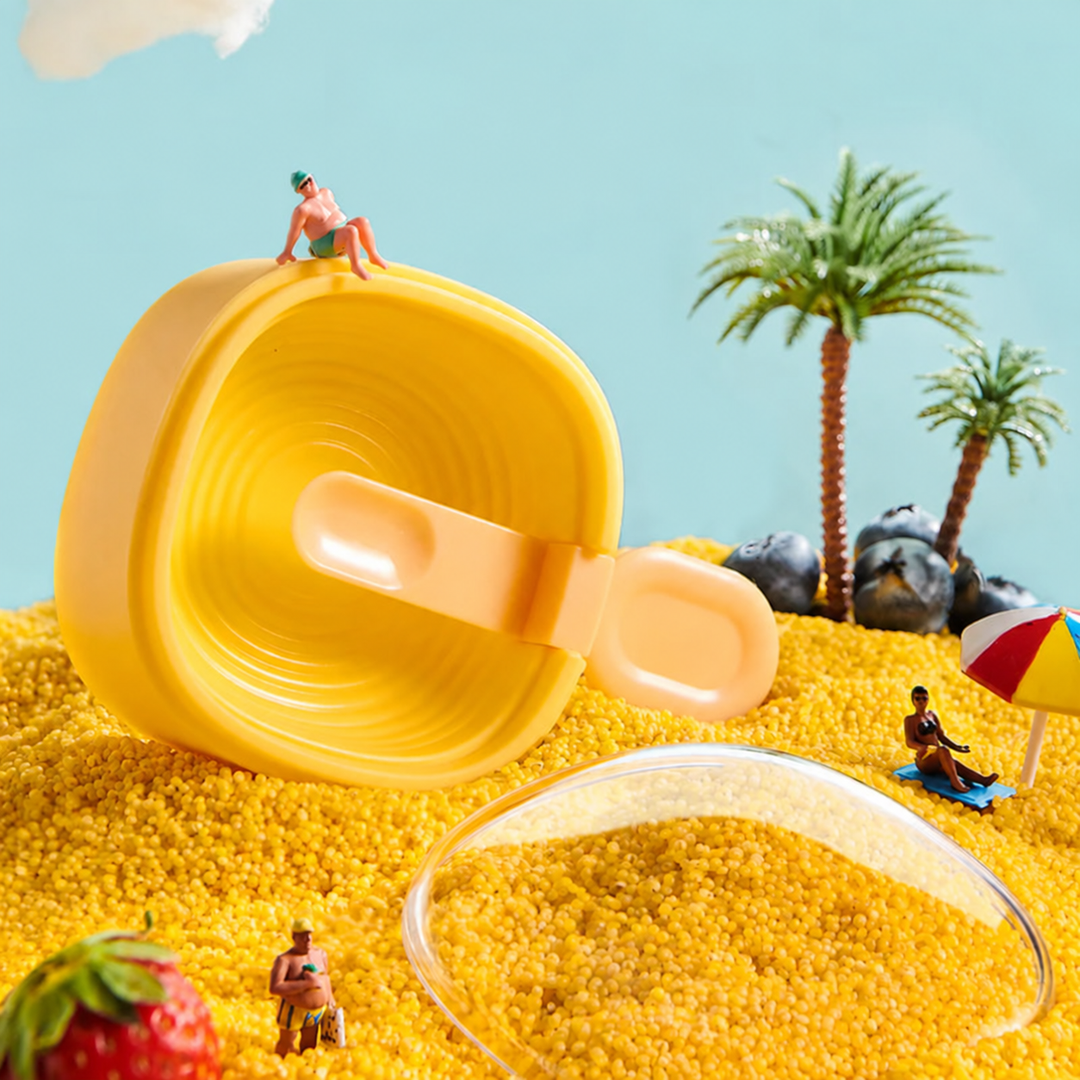 Yellow ice cream mold with a matching spoon and clear lid in a miniature beach scene.