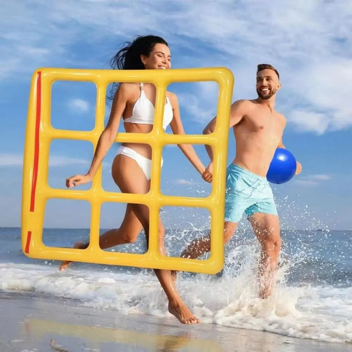 Two adults at the beach carrying a yellow inflatable game grid and a blue ball
