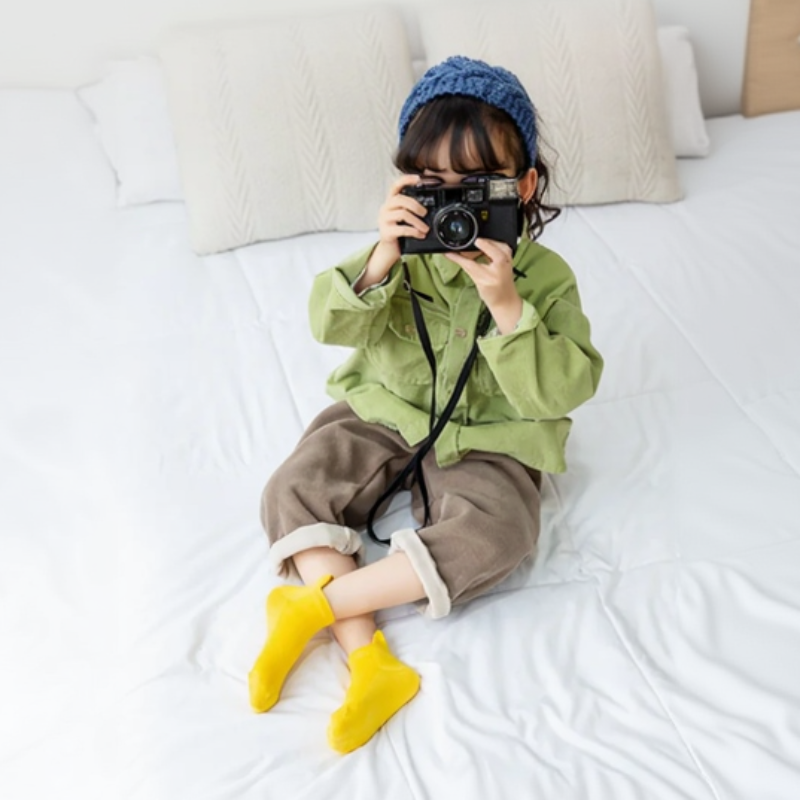 Child wearing yellow low-cut socks while sitting on a bed with a camera