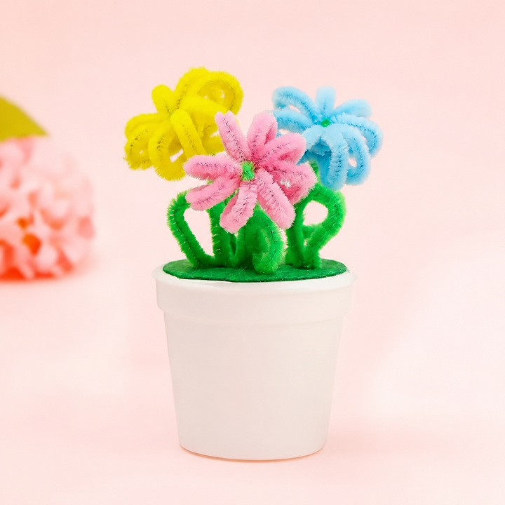 Yellow, pink, and blue fuzzy-wire flowers with curled green leaves in a white pot