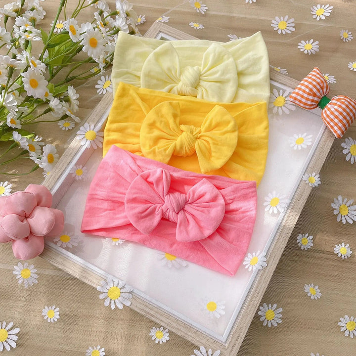 Pale yellow, golden yellow, and pink bow headbands stacked in a frame