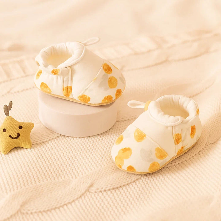 Pair of white baby shoes with yellow printed motifs and elastic openings