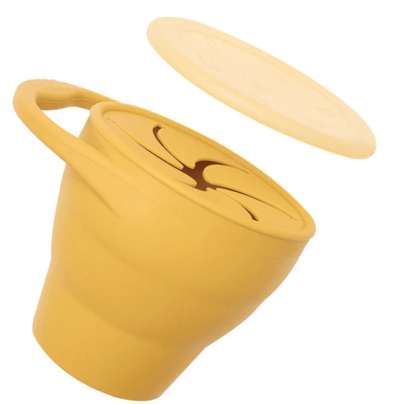 Yellow silicone snack cup with a loop handle, flexible opening, and raised cover