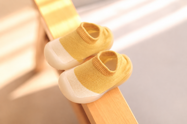 Yellow slip-on baby shoes with ribbed openings and cream toes on a wooden rail.
