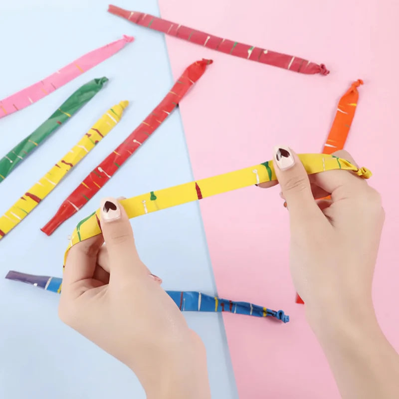 Hands stretching a yellow striped rocket balloon with other colors laid out nearby