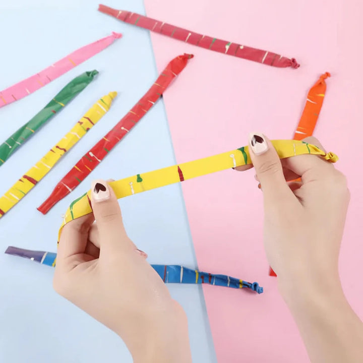 Hands stretching a yellow striped rocket balloon with other colors laid out nearby